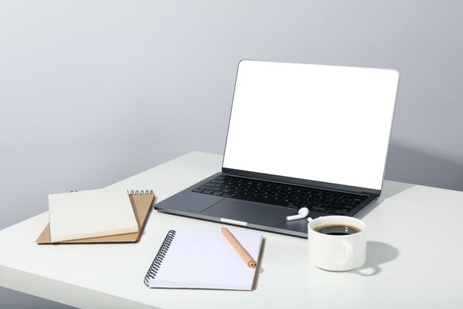Table with open laptop with mockup screen, earbuds, coffee, and blank notebooks