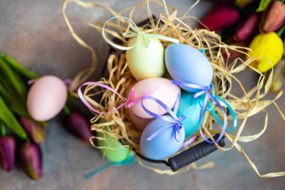 Decorative pastel Easter eggs in straw on table with tulips