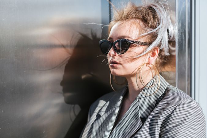 Stylish woman in black sunglasses leaning on metal wall