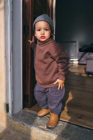 Cute toddler standing near entrance of house and looking at came