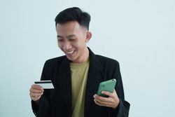 Happy Asian businessman in suit holding blank credit card and smartphone