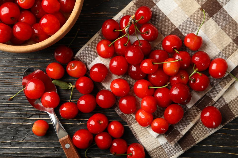 Towel, spoon and bowl with cherry on wooden background, top view