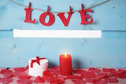 Gift box and the word love spelled out in paper letters hanging on twine with a candle in front