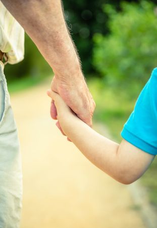 Back view of child and older man holding hand