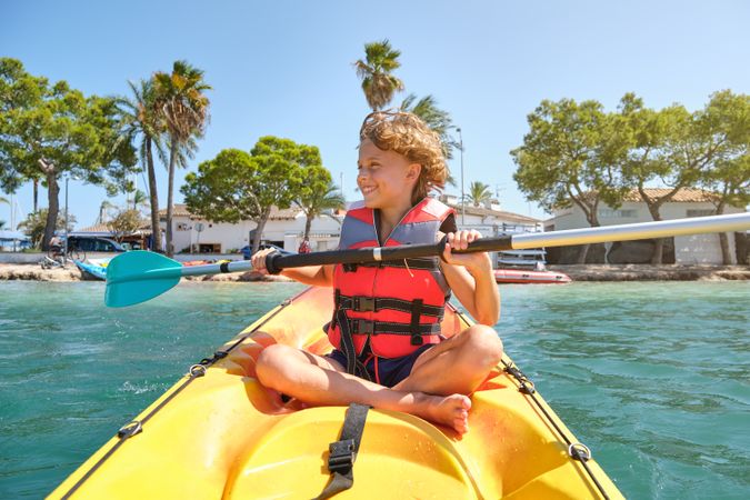 Cheerful kid paddling boat in ocean near beach