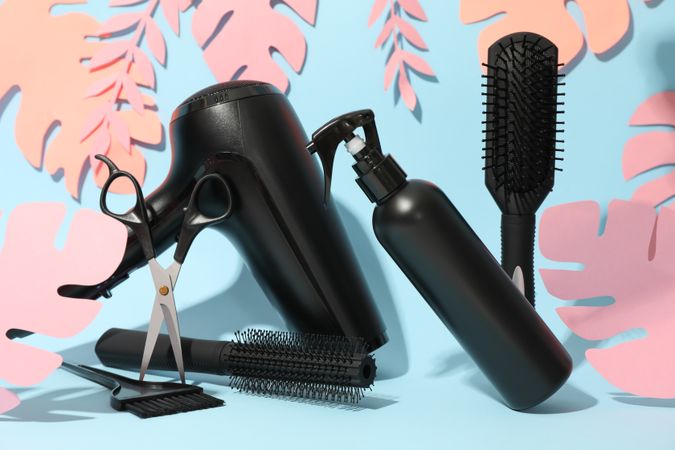 Composition with hairdressing accessories and paper palm leaves on blue background