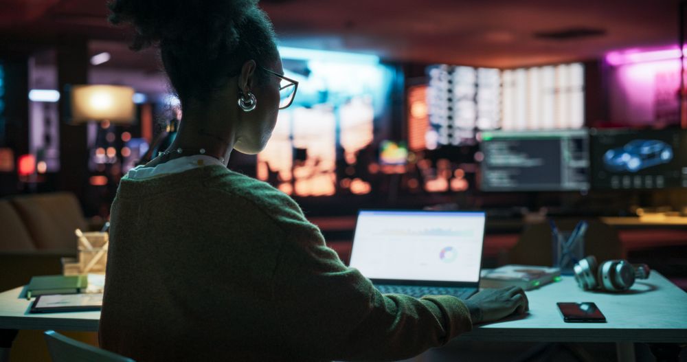 Backview: Motivated Black Female Using Laptop Computer in Creative Agency in the Evening