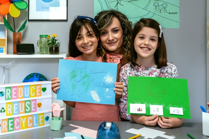 Teacher in classroom looking at camera next to students showing colorful ecological drawings