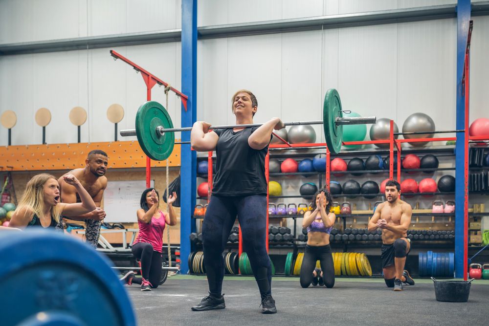 Proud woman weightlifting while her gym mates cheering her on