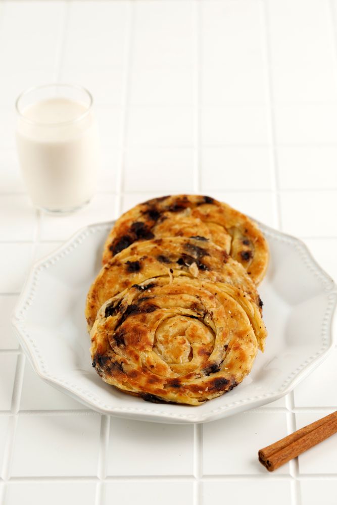 Round plate of sweet raisin cinnamon roti parata or roti canai with milk, vertical