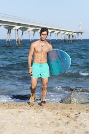 Front of male surfer with blue board in front of the coast