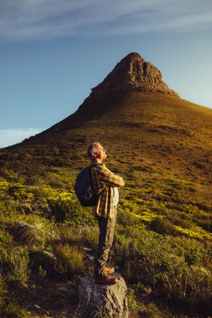 Mature man standing on a rock near a hill wearing a backpack enjoying the view