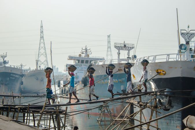 Group of people holding basins over their head walking from ship toward land
