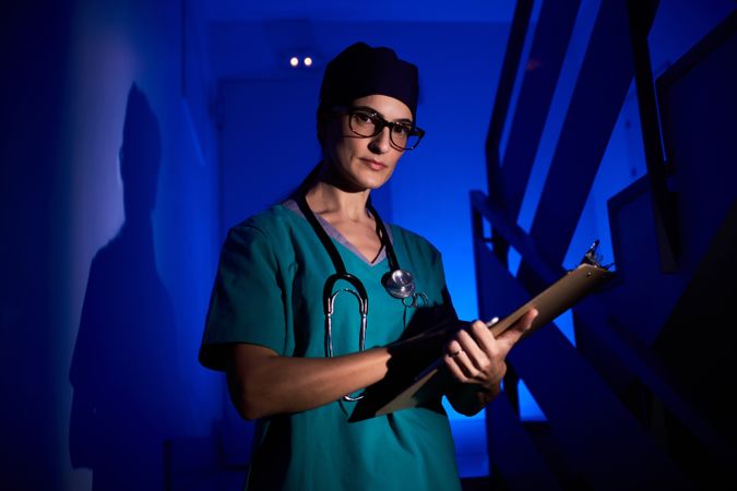Confident woman in scrubs with clipboard standing on staircase