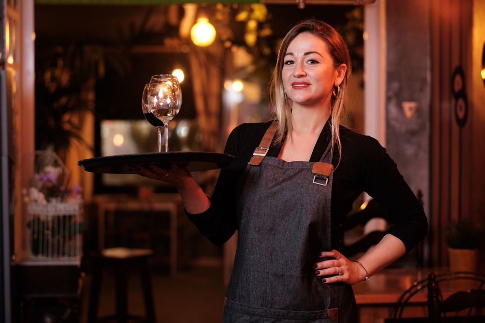 Cheerful waitress holding tray with wineglasses