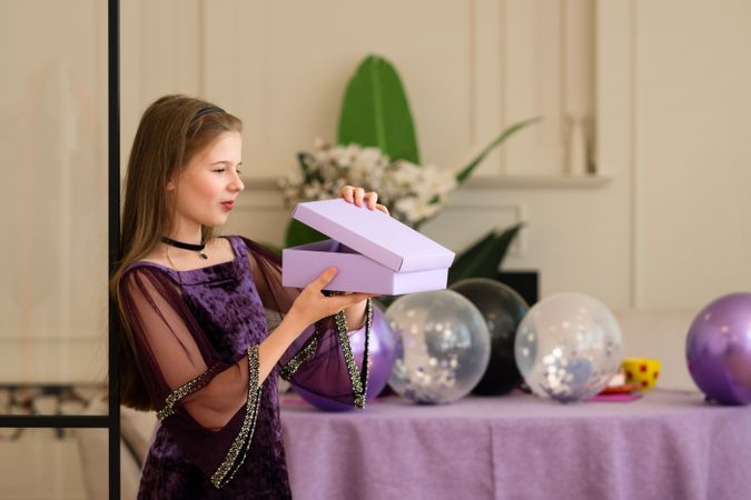 Girl opening gift box at birthday party with balloons