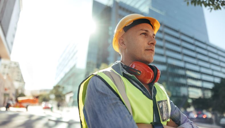 Thoughtful construction worker  standing in the city wearing helmet and safety vest