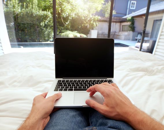 Closeup image of man lying in  bed working on laptop