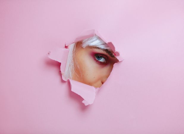 Female with eye makeup peeking through torn paper
