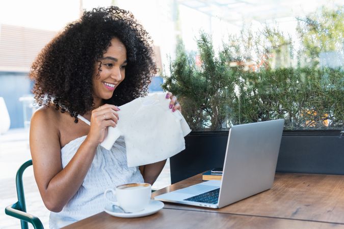 Smiling pregnant Black woman showing baby booties to laptop