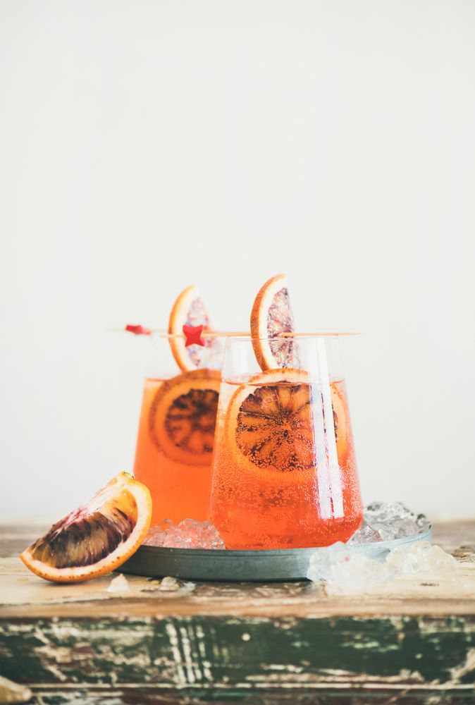 Two glasses of an orange cocktail on board, with blood orange slices, and cocktail picks