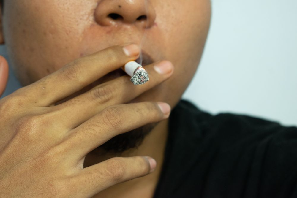 Unrecognizable man holding a burning cigarette to their mouth
