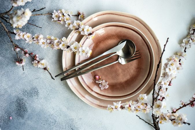 Top view of pink table setting of apricot blossom branches surrounding plates on grey table