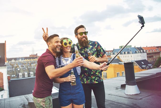 Three friends taking using selfie stick at goofy rooftop party