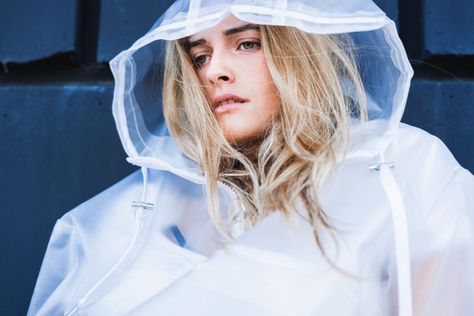 Charming stylish woman in raincoat sitting near wall