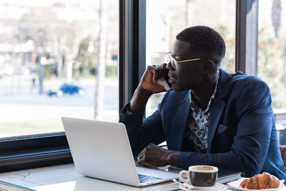 Stylish Black executive on a phone call on mobile phone and laptop in cafe