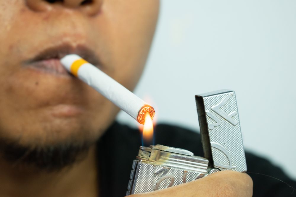 Unrecognizable person lighting a cigarette in their mouth