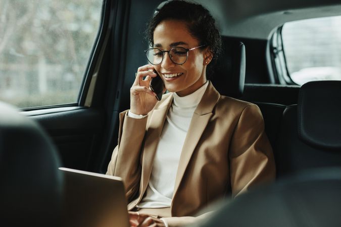 Woman sitting on back seat of car using laptop and phone