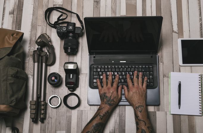 Anonymous photographer using laptop near equipment and stationery
