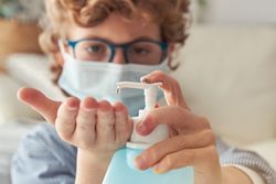 Crop boy in mask applying sanitizer on hand