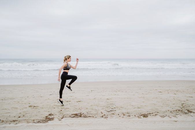 Young female athlete in active wear jogging while jumping at sea beach
