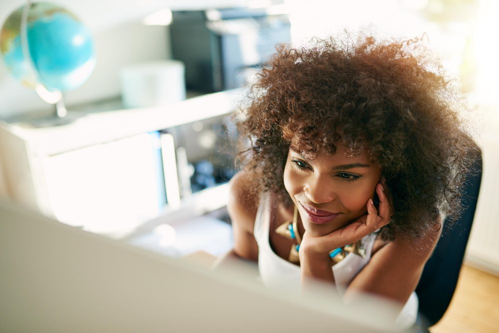 Looking down at curly haired female at her home office desk reading computer screen