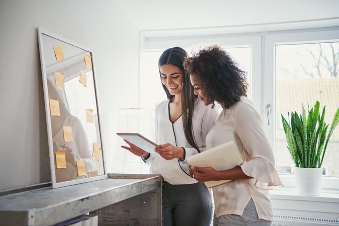 Two cheerful multi-ethnic creative businesswomen with tablet working on