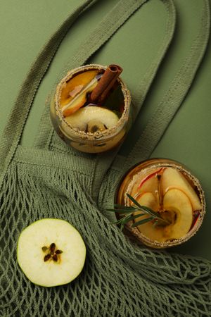 Glasses with apple cider and apple slice on bag on green background, top view