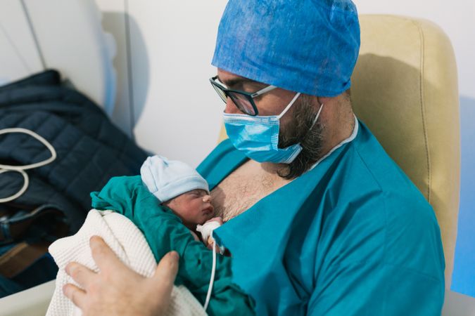 An adult man siting and holding his newborn baby in hospital