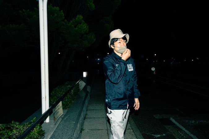 Man with facemask and hat standing outdoor at night