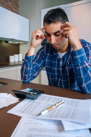 Stressed man with calculator and bills in kitchen, vertical