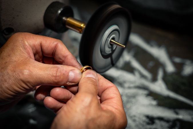 Goldsmith polishing a gold ring jewel in his jewelry workshop. Jeweler hands working in his craftwork studio.