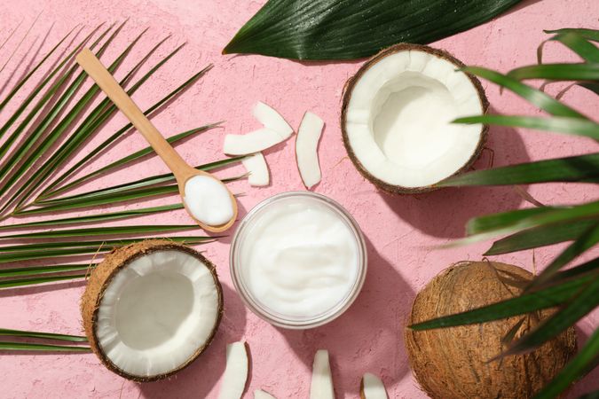 Coconut and cosmetics on pink background, top view