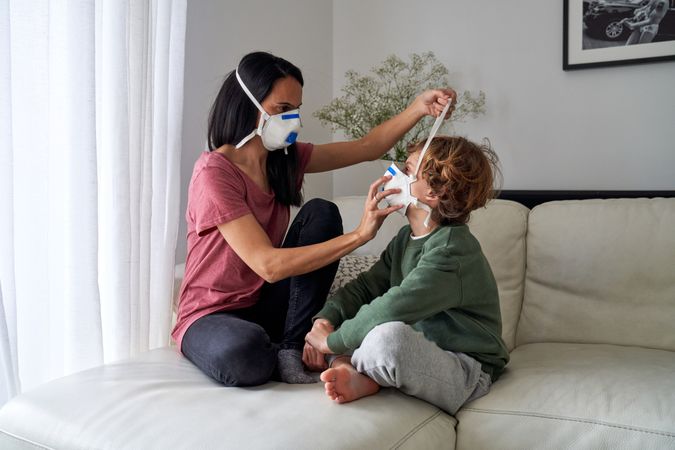 Son and mom wearing protective masks together on couch