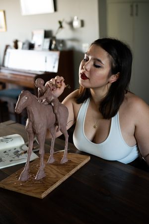 Young focused art student working on clay sculpture with animal anatomy book on table