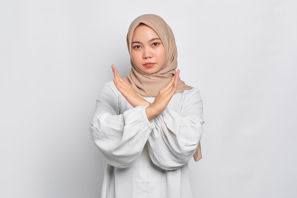 Stern Asian female in headscarf with arms in an “X” over her chest