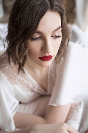 woman with red lips in white dress looking away while sitting on floor beside sofa