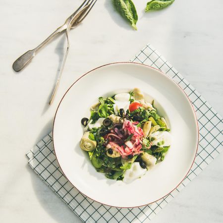 Artichoke salad in bowl, light background with checkered napkin, square crop