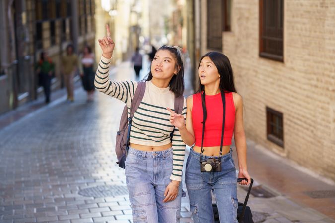 Asian females travelers pointing away while walking on street