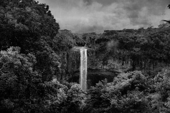 Waterfall surrounded by lush vegetation on cloudy day in monochrome